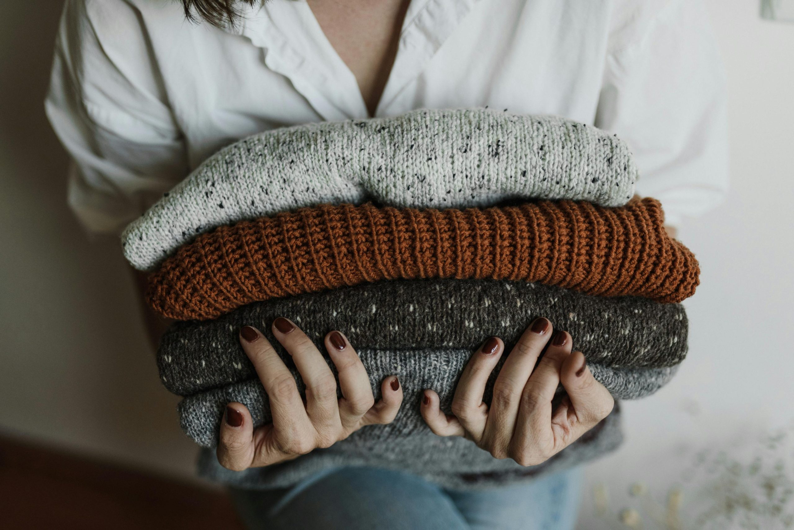woman carrying a stack of folded knitted sweaters